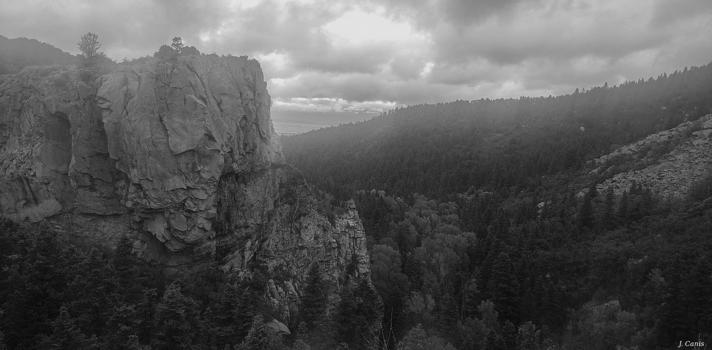 Colorado Canyon Overwatch — dramatic canyon rock face and forested valley under stormy sky, black and white photography by Jon Canis