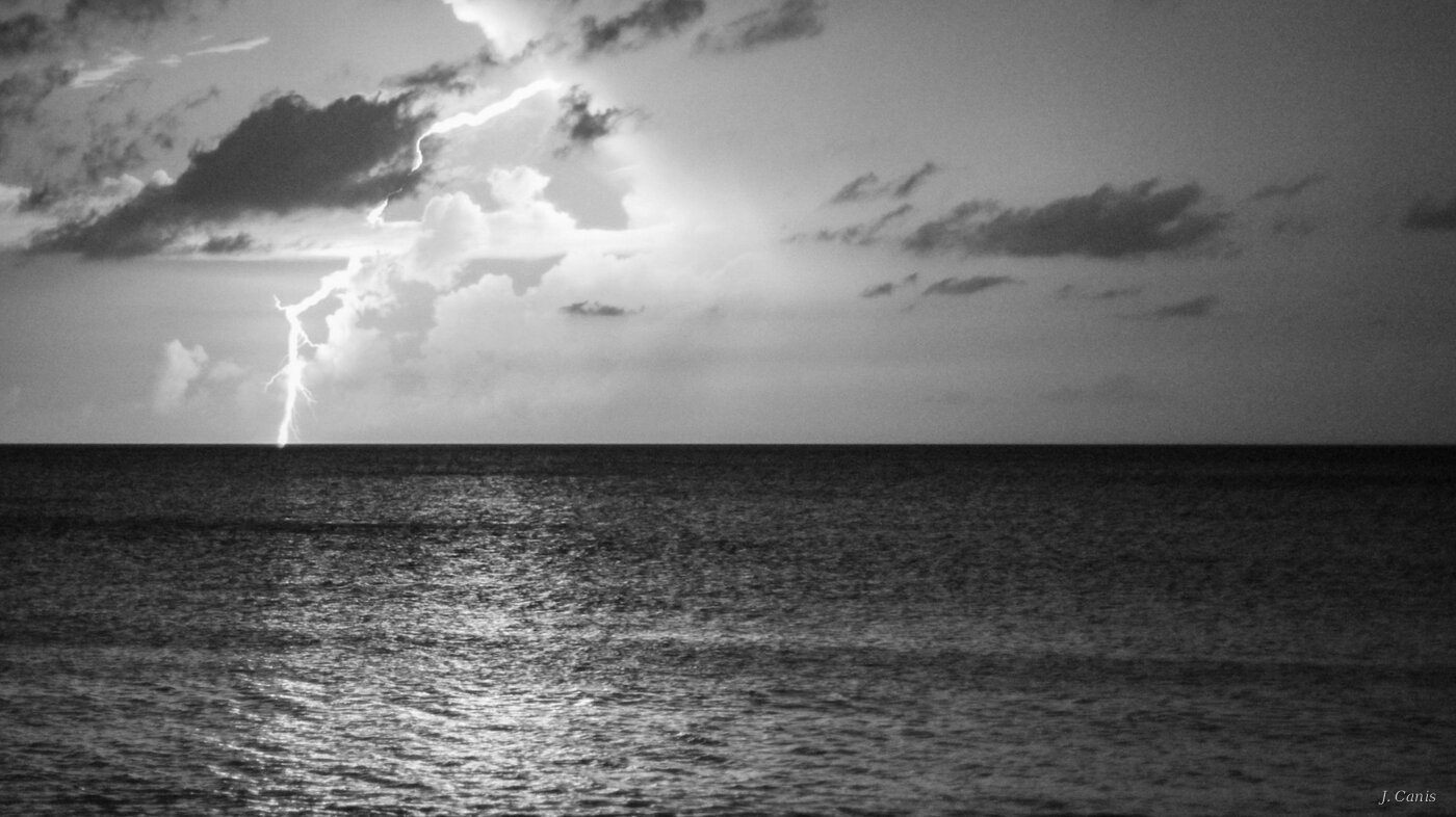 Cayman Lightning — lightning strike over Caribbean Sea at night, black and white photography by Jon Canis